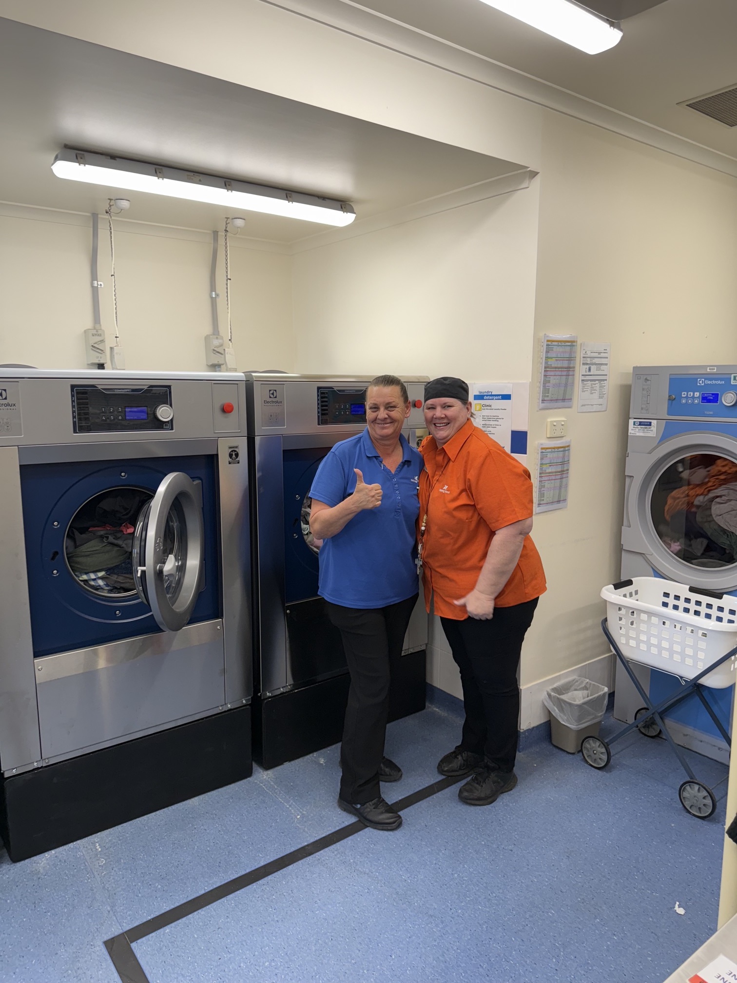 Two laundry staff members standing beside newly installed commercial washer extractors