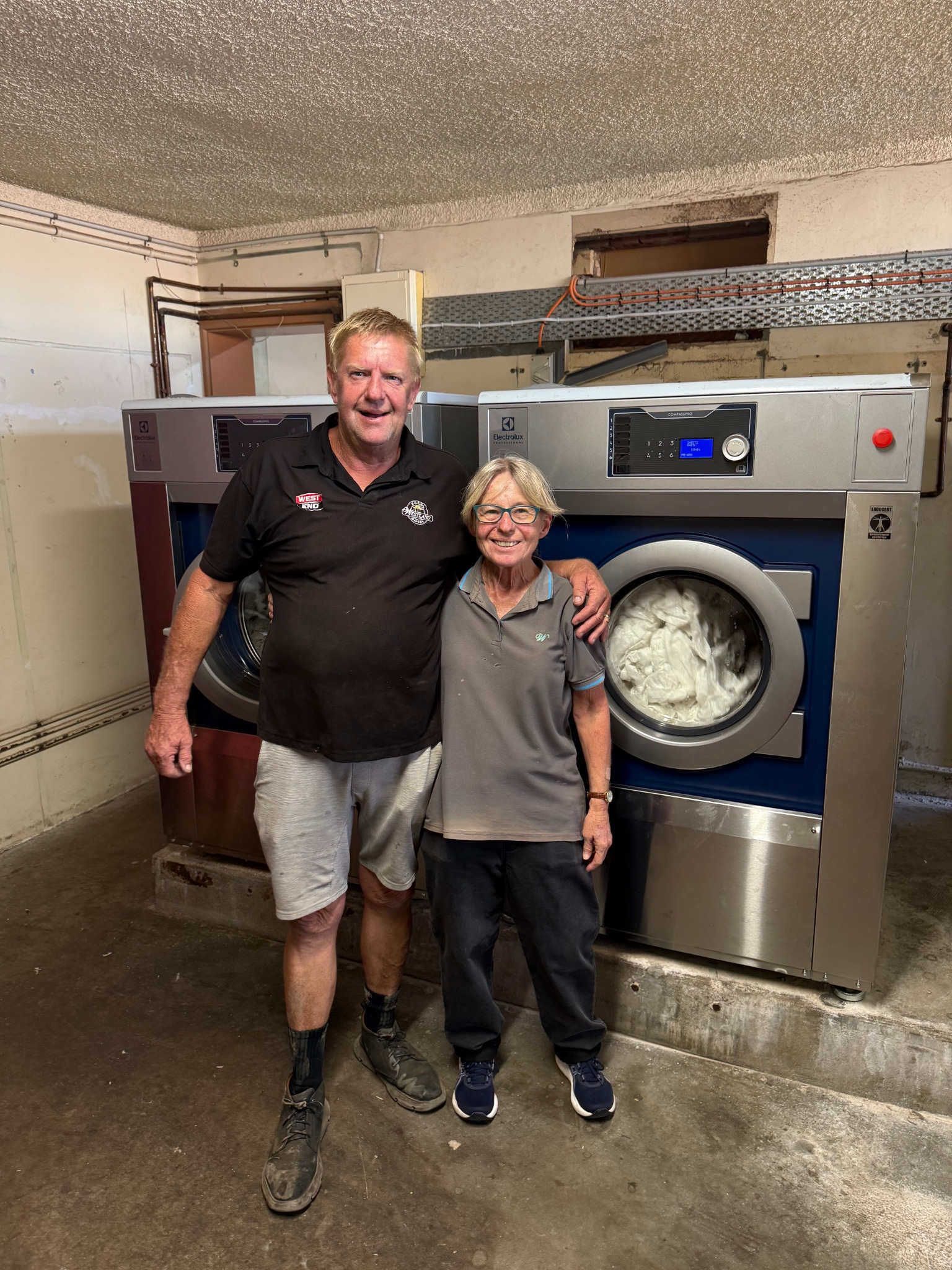 Two people standing in front of newly installed commercial washer extractors in operation