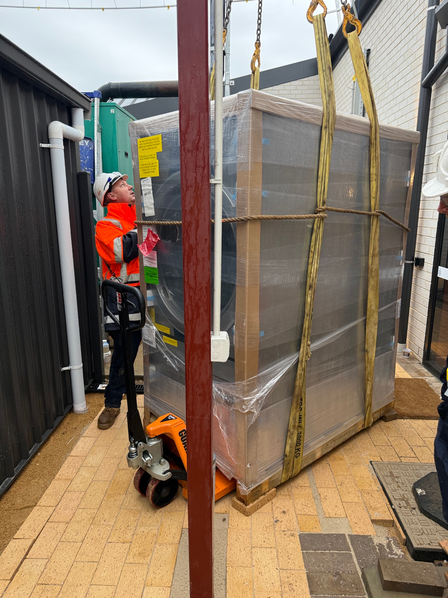 Crated commercial dryer being lifted by crane into a tight access area