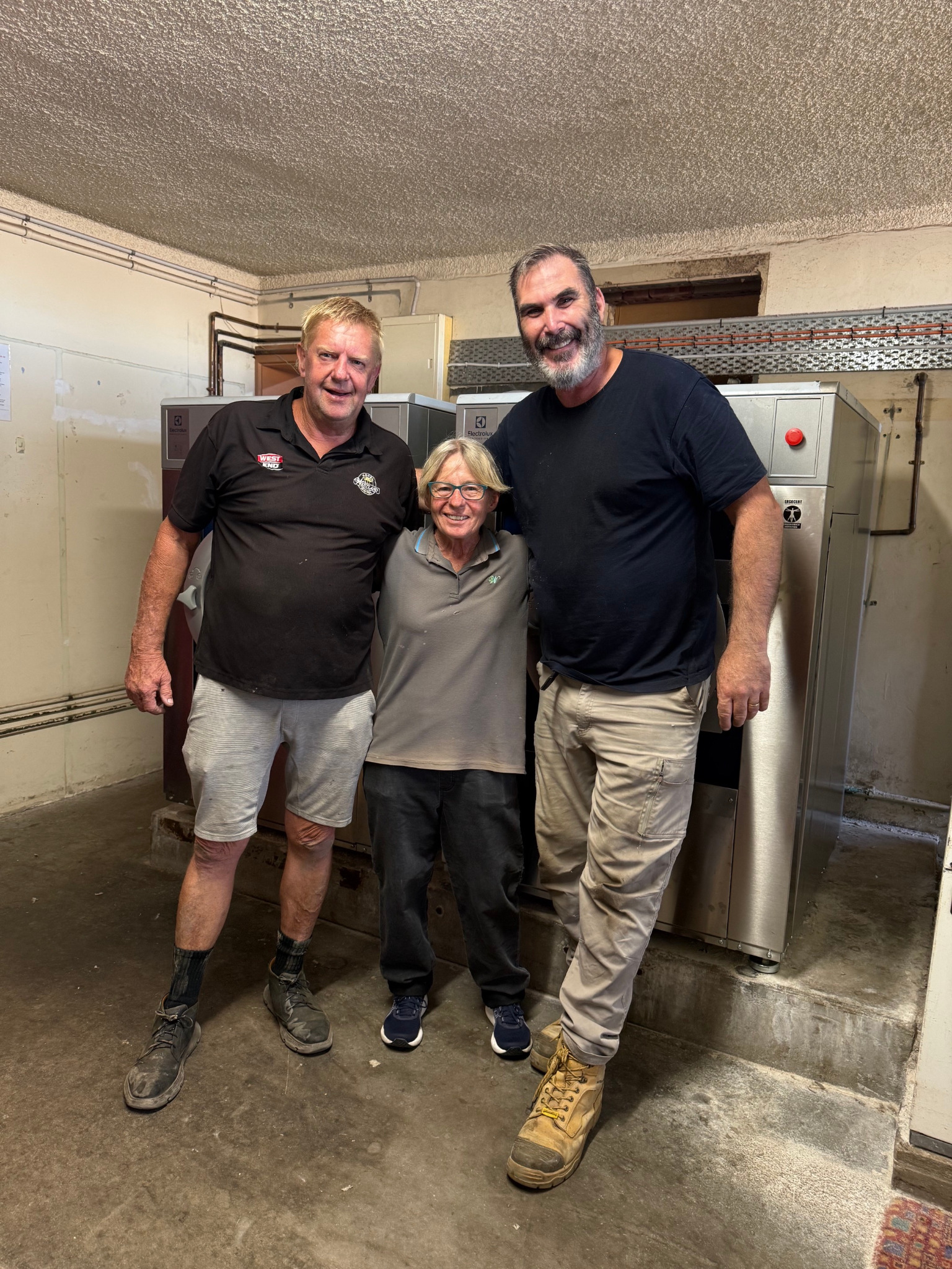 Three people standing together in front of newly installed commercial laundry equipment