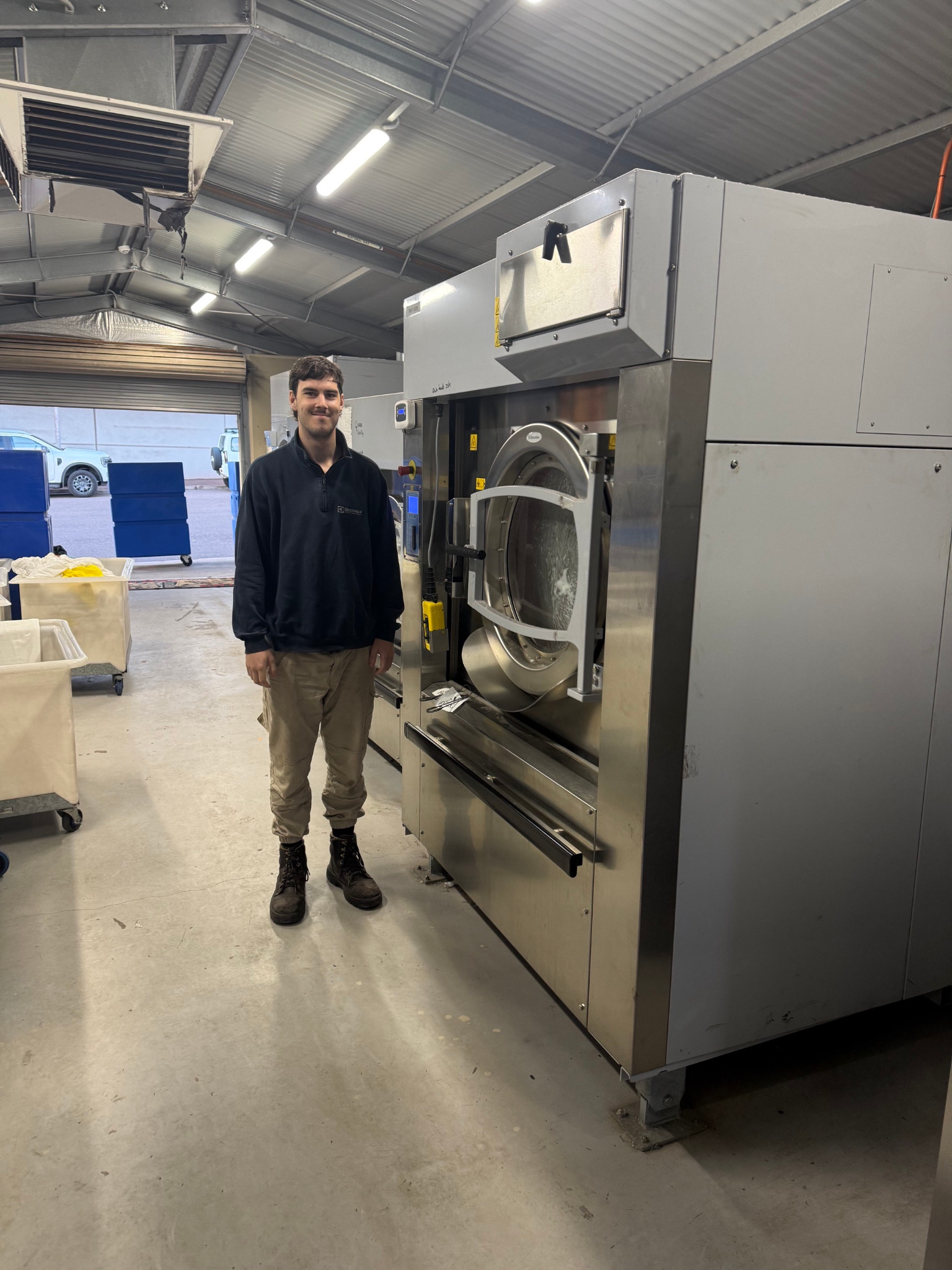 Team member standing beside a large heavy-duty washer extractor, showing its scale
