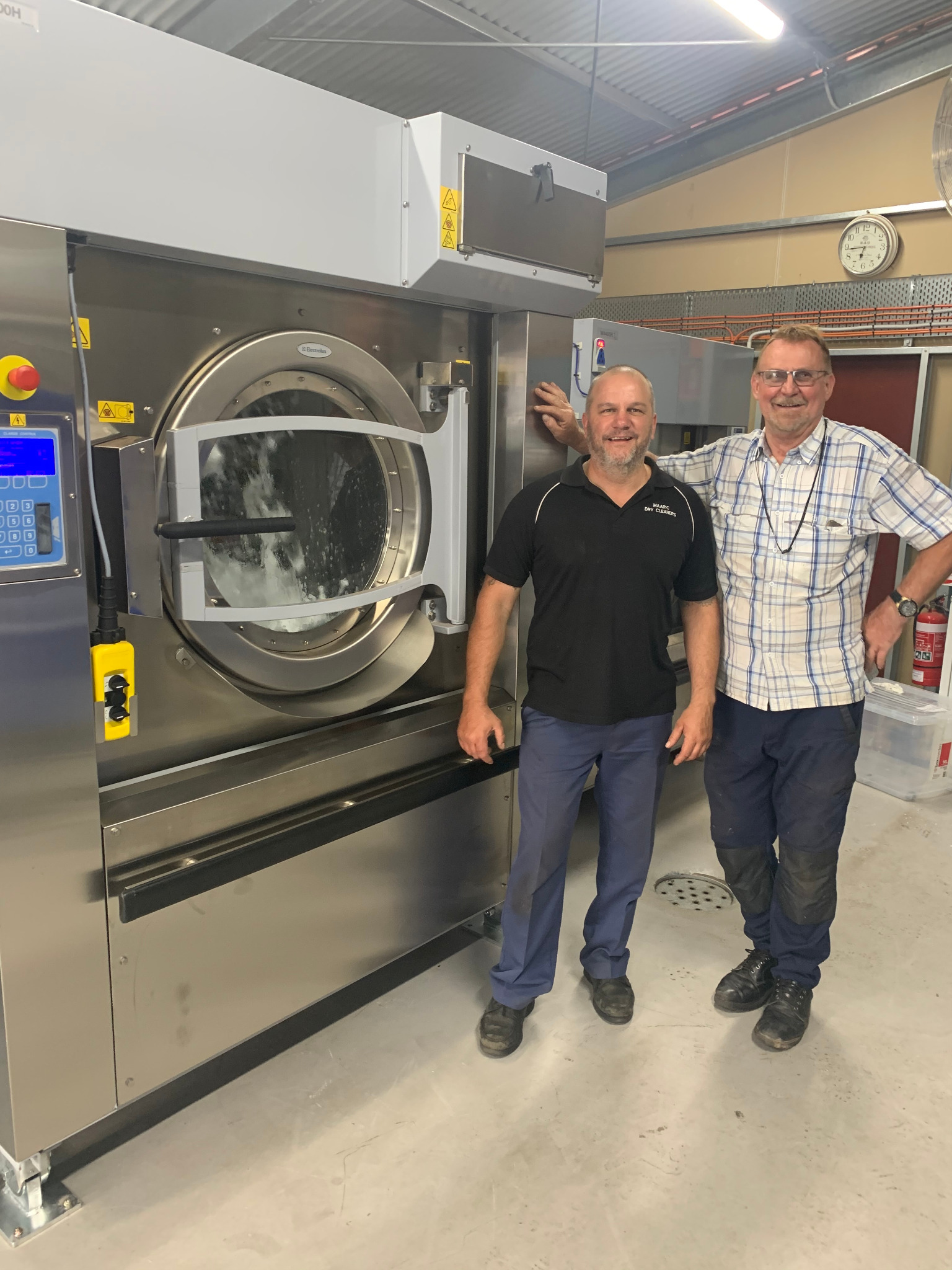 Two people standing beside a large installed heavy-duty washer extractor