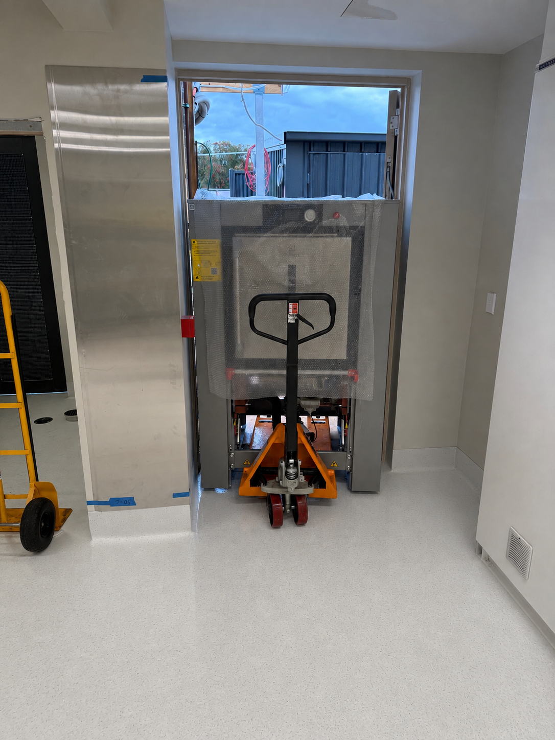 Large barrier washer being moved through a narrow doorway on handling equipment