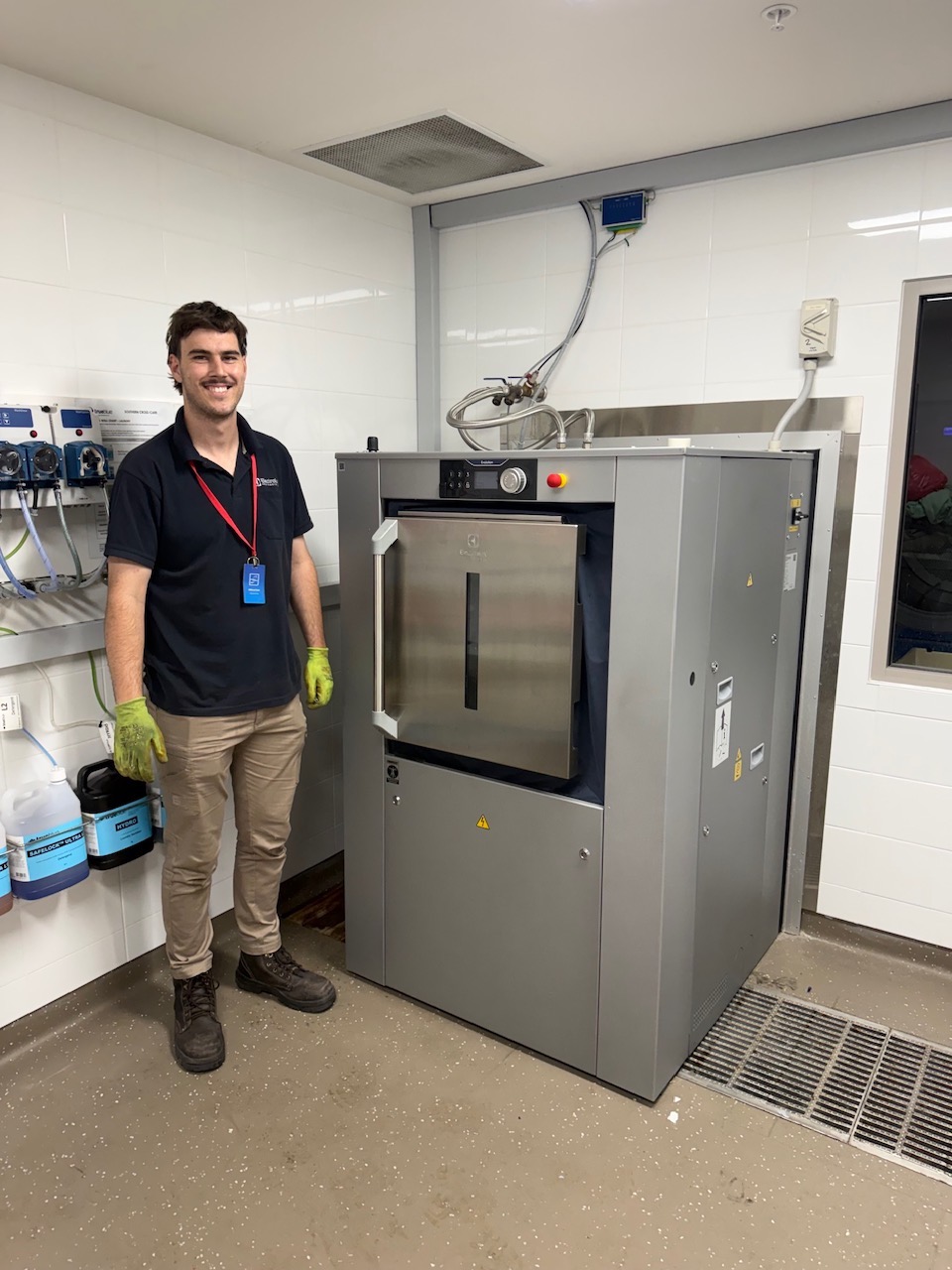Technician standing beside a newly installed barrier washer extractor in an aged care laundry