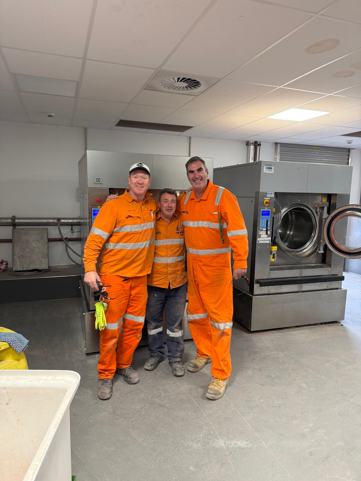 Three people standing together in front of newly installed laundry equipment